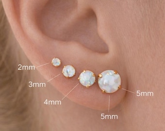 May include: A set of five round, white, iridescent stud earrings set in gold-toned metal prongs. The earrings are labeled with sizes 2mm, 3mm, 4mm, and 5mm, arranged in a row along the earlobe with one additional stud in the upper ear cartilage.