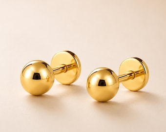 May include: A pair of polished gold-tone ball stud earrings featuring a smooth, spherical front design and a flat circular backing. The earrings have a reflective, metallic finish and a simple, clean construction with a post and secure back mechanism.