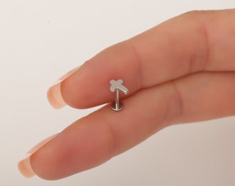 May include: Silver cross body jewelry for a piercing. The cross is small and simple.