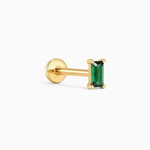 May include: A gold-toned labret stud earring featuring a rectangular baguette-cut emerald green gemstone set in a four-prong metal frame. The jewelry piece includes a smooth, cylindrical post and a flat, circular disc backing for secure placement.