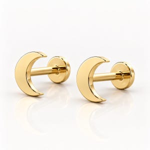May include: A pair of gold-toned flat back stud earrings, each featuring a crescent moon design. The earrings have a smooth, polished finish and a straight post with a circular backing, presented as two separate pieces on a white surface.