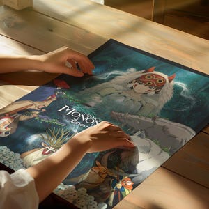 K&ouml;nnte beinhalten: Ein Poster mit Kunstwerken aus dem Animationsfilm "Prinzessin Mononoke". Das Poster zeigt ein zentrales Bild einer Figur mit Maske und Wolf. Der Titel "Prinzessin Mononoke" ist auf Englisch und Japanisch zu sehen.