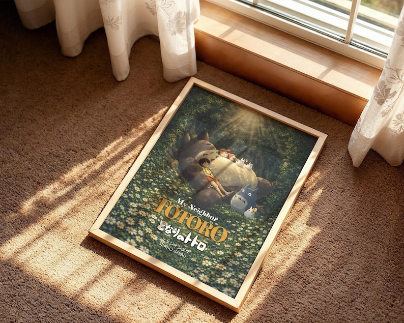 K&ouml;nnte beinhalten: Ein gerahmter Druck des Animationsfilms "Mein Nachbar Totoro" mit den Charakteren Totoro, Mei und dem Katzenbus. Das Kunstwerk spielt in einem Wald mit einem Feld wei&szlig;er Blumen, mit dem Titel in goldfarbenen Buchstaben.