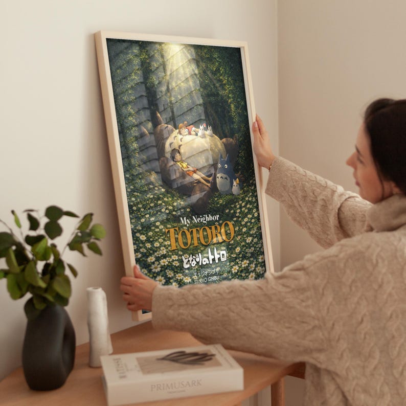 K&ouml;nnte beinhalten: Gerahmtes Poster des Zeichentrickfilms "Mein Nachbar Totoro". Das Kunstwerk zeigt Totoro, einen gro&szlig;en Waldgeist, mit Kindern und anderen Kreaturen in einem gr&uuml;nen Wald. Das Poster hat einen wei&szlig;en Rahmen.