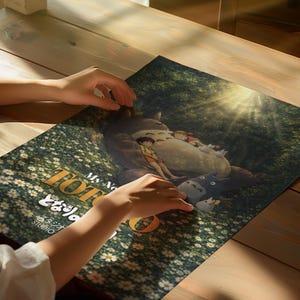 K&ouml;nnte beinhalten: Ein Poster mit einer Szene aus dem Zeichentrickfilm "Mein Nachbar Totoro". Das Kunstwerk zeigt Totoro mit Kindern in einer Waldszene, mit dem Titel in Englisch und Japanisch. Das Poster liegt auf einem Holztisch.