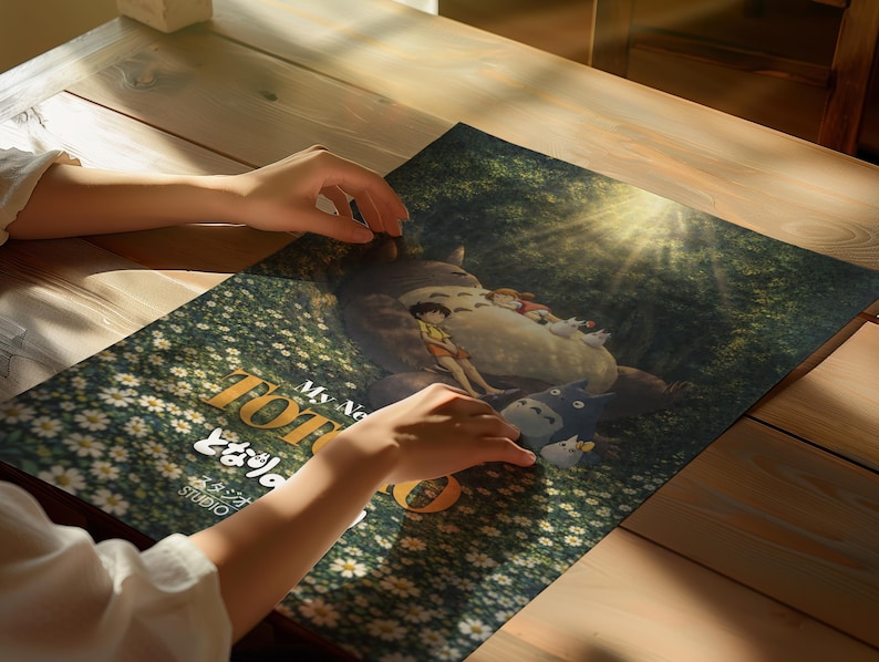 K&ouml;nnte beinhalten: Ein Poster mit einer Szene aus dem Zeichentrickfilm "Mein Nachbar Totoro". Das Kunstwerk zeigt Totoro mit Kindern in einer Waldszene, mit dem Titel in Englisch und Japanisch. Das Poster liegt auf einem Holztisch.