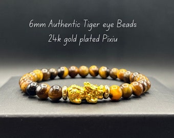 Op de afbeelding: Een armband met 6 mm tijgeroog kralen en een vergulde Pixiu bedel. De tekst op de afbeelding luidt "6mm Authentic Tiger eye Beads 24k gold plated Pixiu". De armband wordt gepresenteerd op een zwarte ondergrond.