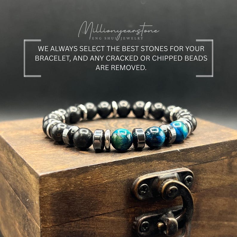 May include: A beaded bracelet with black and blue-green stones, and silver-colored spacers. The bracelet is displayed on a wooden box. Text on the image reads: "Millionyearstone Feng Shui Jewelry" and "WE ALWAYS SELECT THE BEST STONES FOR YOUR BRACELET, AND ANY CRACKED OR CHIPPED BEADS ARE REMOVED."