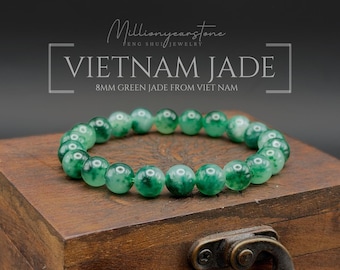 May include: A bracelet made of 8mm green jade beads. The text on the image reads: Millionyearstone FENG SHUI JEWELRY VIETNAM JADE 8MM GREEN JADE FROM VIET NAM. The beads are round, polished, and feature varying shades of green with dark inclusions.