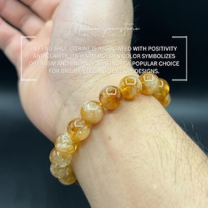 May include: A bracelet of golden citrine beads. The beads are round and have a warm, amber color. The bracelet is worn on a wrist. Text in the image states that citrine symbolizes optimism and balance.