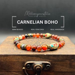 Puede incluir: Una pulsera bohemia de cornalina con cuentas de 6 mm. La pulsera presenta cuentas naranjas, marrones y doradas con detalles decorativos. El texto de la imagen dice "Millionyearstone Feng Shui Jewelry", "Carnelian Boho", "Real Feng Shui" y "Real Handmade".