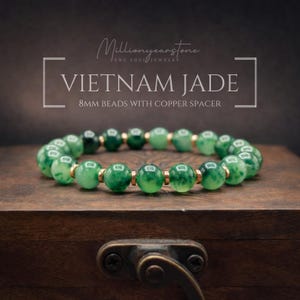 May include: A jade bracelet with 8mm beads and copper spacers. The bracelet is made of green jade beads and is displayed on a wooden surface. The text "VIETNAM JADE" is visible in the image.