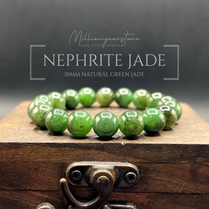 May include: A bracelet of Nephrite Jade beads, each 10mm in diameter, displayed on a wooden box. The beads are a vibrant green colour with natural variations. The text "NEPHRITE JADE" and "10MM NATURAL GREEN JADE" is visible in the image.
