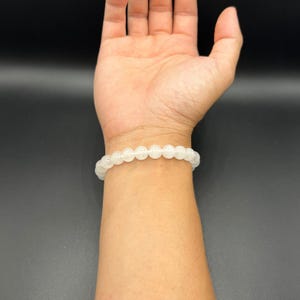 Op de afbeelding: Een witte kralen armband gedragen op een pols. De armband is gemaakt van kleine, ronde kralen die aan elkaar geregen zijn op een doorzichtig elastiek.