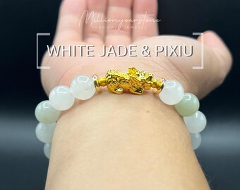 Może przedstawiać: Bransoletka z białego jadeitu ze złotym urokiem Pixiu. Bransoletka posiada okrągłe, jasnozielone i białe koraliki z jadeitu. Tekst "WHITE JADE & PIXIU" jest wyświetlany białą czcionką.