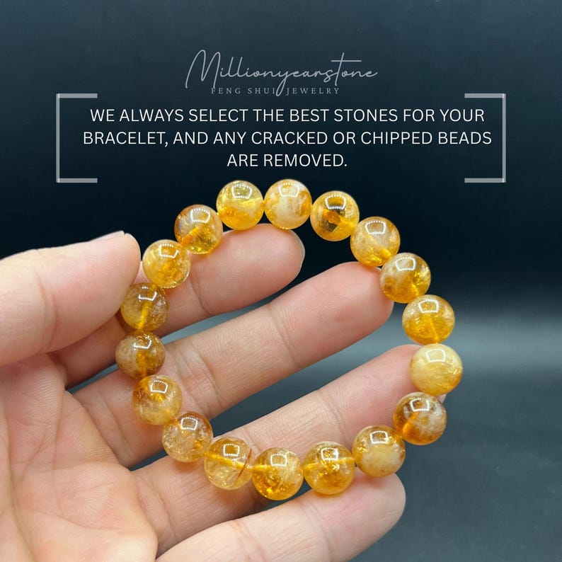 May include: A bracelet of golden-yellow, round gemstone beads is held in a hand. The beads have a translucent quality, with variations in color and texture. The bracelet is displayed against a dark background. Text on the image reads: "Millionyearstone FENG SHUI JEWELRY".