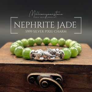 Op de afbeelding: Een Nephrite Jade armband met een zilveren Pixiu bedel. De armband heeft ronde, lichtgroene jade kralen. De Pixiu bedel is ingewikkeld gedetailleerd. De tekst op de afbeelding luidt "Millionyearstone Feng Shui Jewelry" en "Nephrite Jade S999 Silver Pixiu Charm."