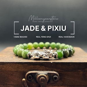 Könnte beinhalten: Ein Armband aus Jade und Pixiu mit 7,5 mm großen, grünen Jade-Perlen. Das Armband hat einen silbernen Pixiu-Anhänger und wird auf einer Holzoberfläche präsentiert. Der Text auf dem Bild lautet "Jade & Pixiu", "Real Feng Shui".