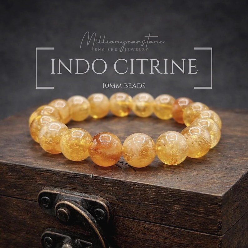 May include: A bracelet of Indo Citrine beads, each 10mm in diameter, displayed on a wooden surface. The beads are a translucent yellow-orange color. The text "INDO CITRINE" and "10MM BEADS" are visible.