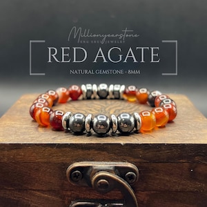 Puede incluir: Pulsera de ágata roja con cuentas de piedras preciosas naturales de 8 mm. La pulsera presenta cuentas rojas y negras alternas con detalles metálicos plateados. El texto "Red Agate" se muestra encima.