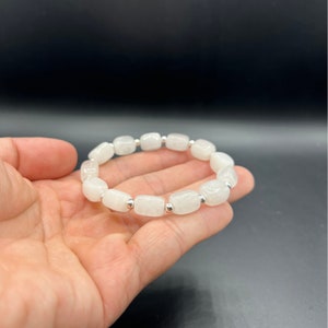 May include: White gemstone bracelet with silver beads. The bracelet is made of round, white stones with a slightly textured surface.