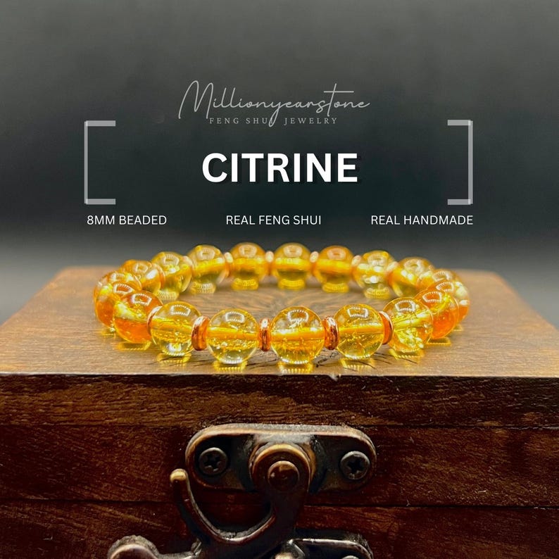 May include: A Citrine beaded bracelet, 8mm, displayed on a wooden box. The bracelet features translucent, golden-yellow beads. Text on the image reads "Citrine", "Real Feng Shui", and "Real Handmade". The jewelry is from Millionyearstone.