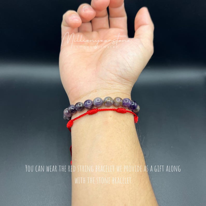 May include: A red string bracelet with a purple and black stone bracelet on top of it. The text "YOU CAN WEAR THE RED STRING BRACELET WE PROVIDE AS A GIFT ALONG WITH THE STONE BRACELET" is visible on the image.