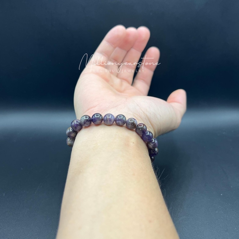 May include: A purple amethyst gemstone bracelet with a silver clasp. The bracelet is on a person's wrist.