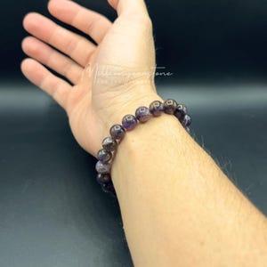 May include: A purple amethyst gemstone bracelet with round beads. The bracelet is on a person's wrist.