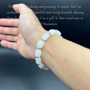 May include: White gemstone bracelet with silver beads. The bracelet is on a person's wrist.