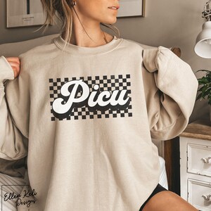 May include: A beige sweatshirt with a black and white checkered design and the word "Picu" in a retro font.