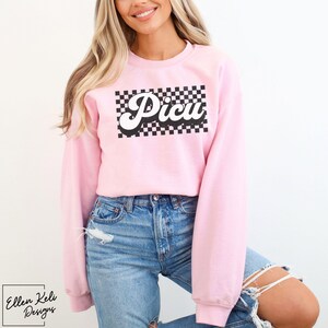May include: A pink sweatshirt with a black and white checkered design and the word "Picu" in a retro font.