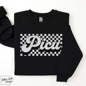 May include: Black sweatshirt with a white checkered pattern and the word "Picu" in a retro, white, cursive font.