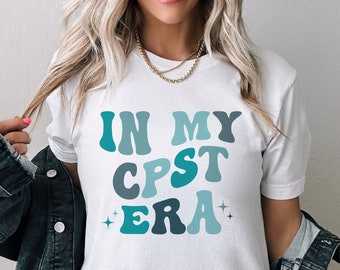 Pode incluir: Camiseta branca com o texto "In My CPST Era" em letras azuis e azul-turquesa com uma fonte retrô.