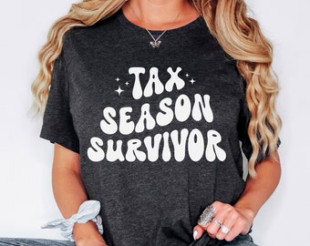 Könnte beinhalten: Ein dunkelgraues T-Shirt mit dem Text "Tax Season Survivor" in weißer, retro-artiger Schrift. Der Text ist von kleinen weißen Sternen umgeben.