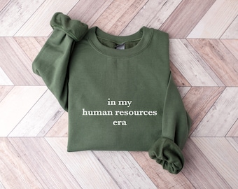 May include: A green sweatshirt with the text "in my human resources era" printed in white on the front.