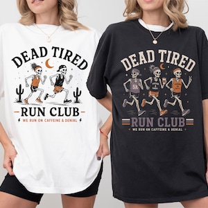 May include: A white t-shirt and a black t-shirt featuring a graphic of skeletons running. The white shirt shows two skeletons with the text DEAD TIRED RUN CLUB WE RUN ON CAFFEINE & DENIAL. The black shirt shows three skeletons with the same text.