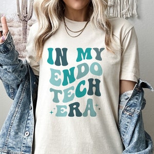 May include: A white t-shirt with the text "In My Endo Tech Era" in blue and green retro-style lettering.