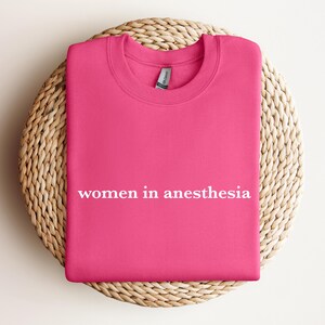 Peut inclure: Sweat-shirt rose avec le texte "women in anesthesia" en lettres blanches.