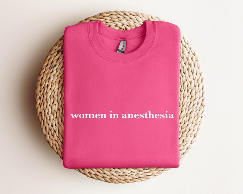 Peut inclure: Sweat-shirt rose avec le texte "women in anesthesia" en lettres blanches.