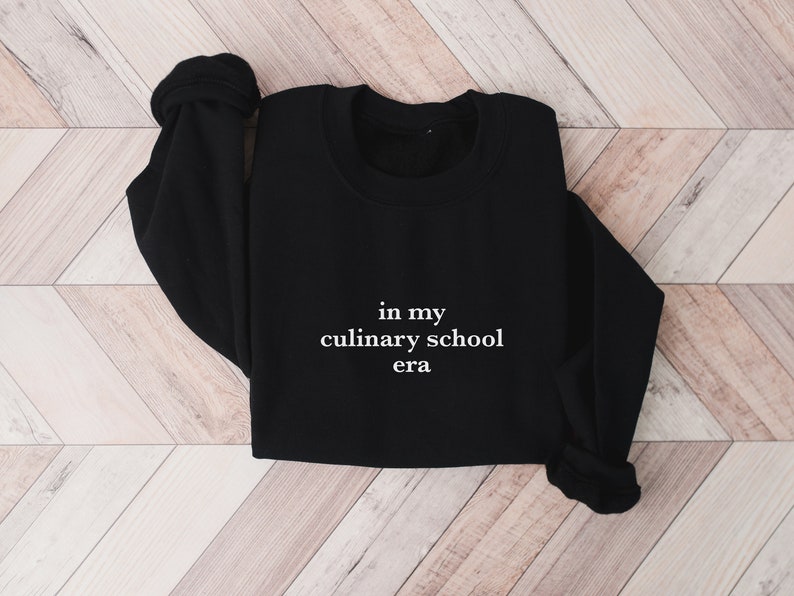 May include: Black sweatshirt with white text that reads "in my culinary school era".