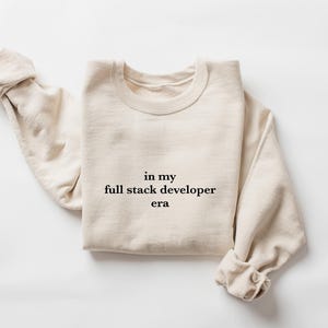 A beige sweater with the text "in my full stack developer era" printed on it.
