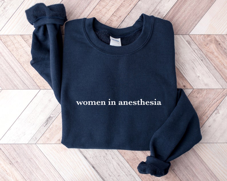 Peut inclure: Un sweat-shirt bleu marine avec le texte "women in anesthesia" imprim&eacute; en blanc sur le devant.
