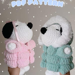 May include: Two crocheted stuffed toys in the shape of a dog wearing winter coats. The dog on the left is wearing a pink coat and the dog on the right is wearing a teal coat.  The text "PDF PATTERN" is at the top of the image.
