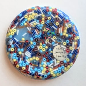 May include: A round, blue, white, yellow, and red resin coaster with a blue and white cartoon character and the text "Ohana means family".