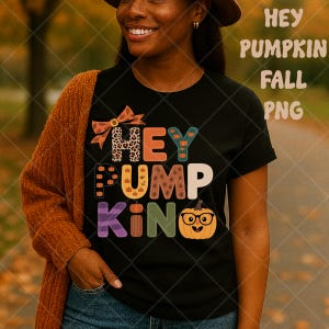May include: Black t-shirt with the words "HEY PUMPKIN KING" in colorful, patchwork-style letters and a pumpkin wearing glasses. The shirt has a fall theme, with a bow and pumpkins incorporated into the design.