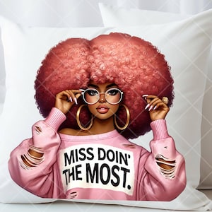 May include: White decorative pillow featuring a stylish illustration of a woman with large, red curly hair, gold hoop earrings, and glasses. She wears a pink distressed sweatshirt with the text "MISS DOIN' THE MOST."