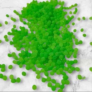 May include: A large quantity of bright green confetti, scattered on a white surface. The confetti is made of small, round pieces of paper.