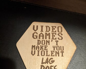 Könnte beinhalten: Ein Untersetzer aus Holz mit dem Text "VIDEO GAMES DON'T MAKE YOU VIOLENT LAG DOES" in einer Pixel-Schriftart.
