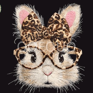 May include: Embroidered image of a bunny face with a leopard print bow, glasses, and ear accents. The bunny has a pink nose and ears, and the glasses have a brown frame. The background is black. The image includes the text "Tayler Willim" in a circular logo.